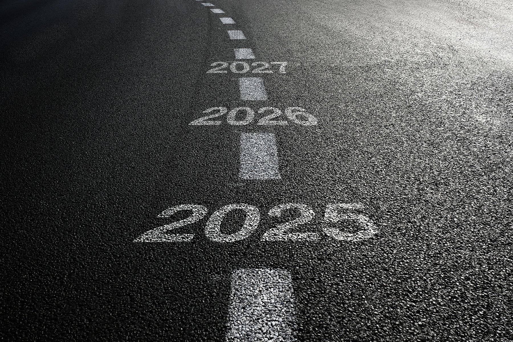 A closeup of as asphalt road with the years 2025, 2026, and 2027 painted on it.