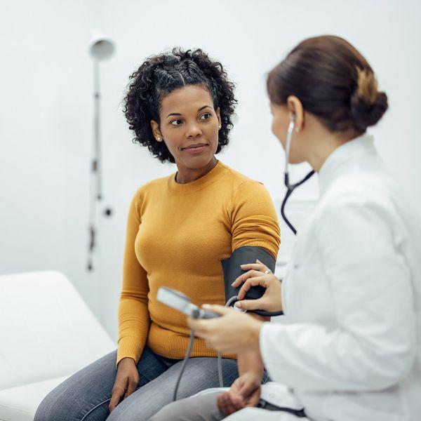 A doctor uses a stethoscope and blood pressure cuff to take a female patient's blood pressure.