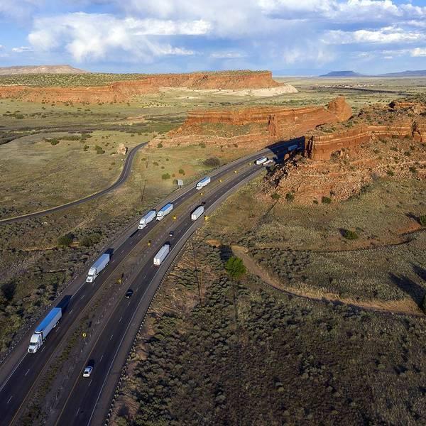 A drone-style image of multiple semi-trucks driving through a Utah landscape against blue skies.