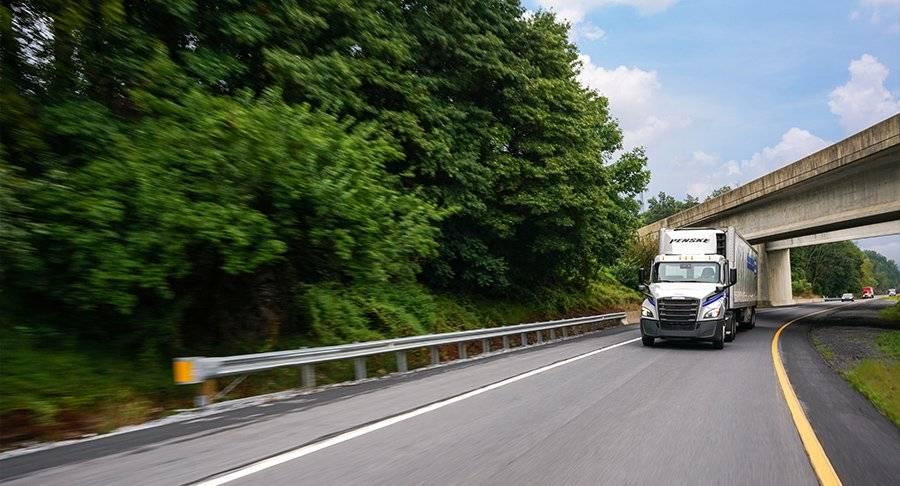 A Penske tractor and refrigerated trailer drive on a road.