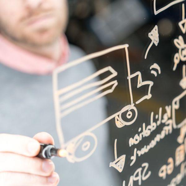 A person uses a marker to draw on a clear whiteboard.