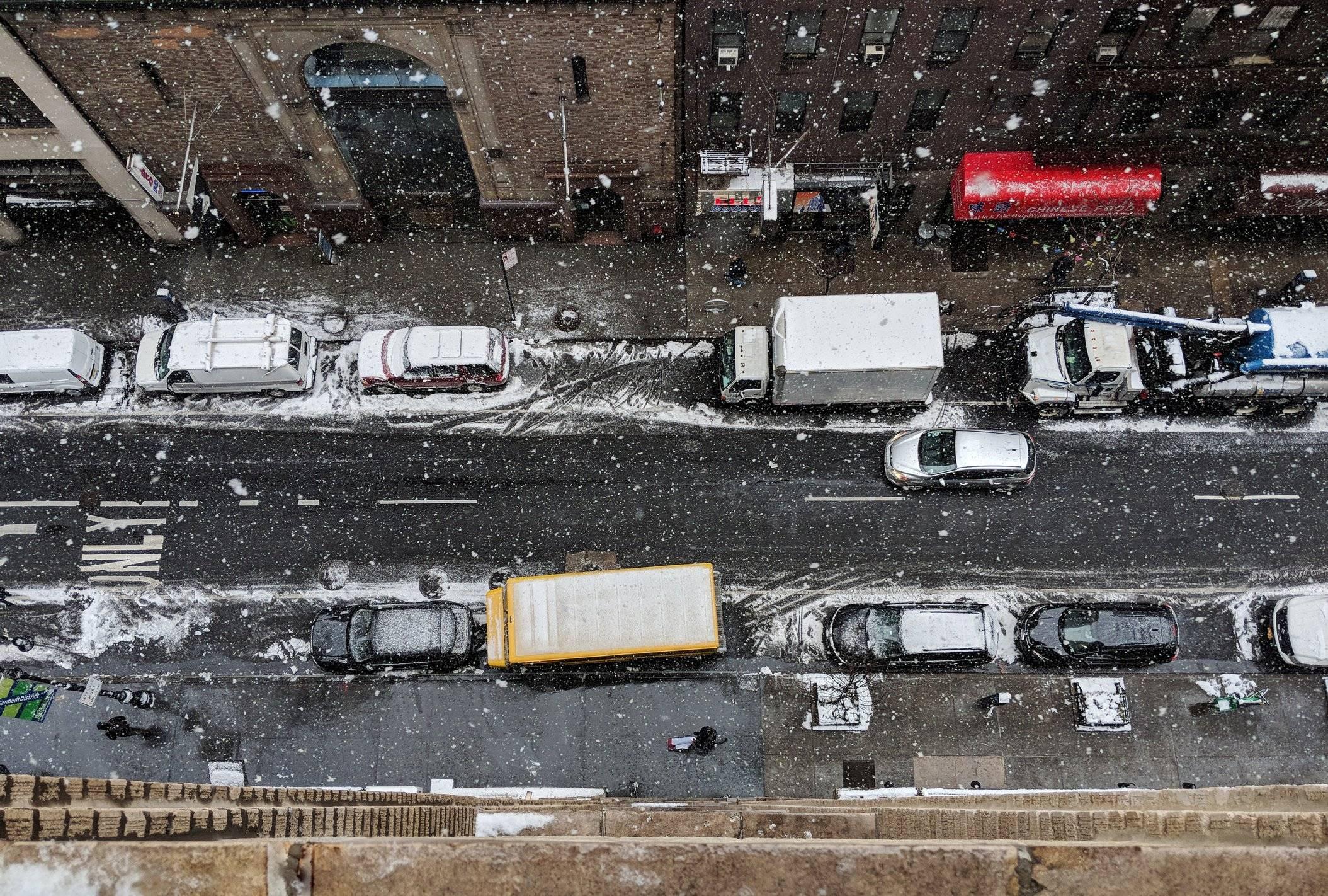 A snowy city street from above, crowded with cars and trucks.
