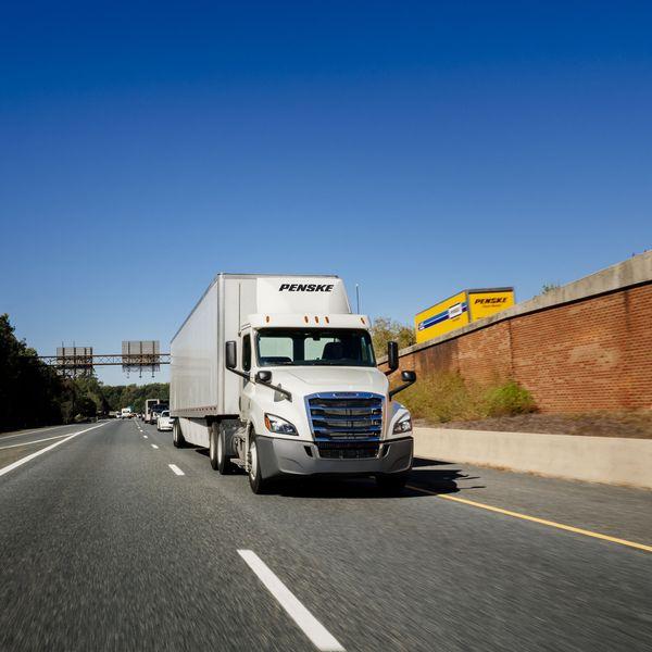 A white Penske semi-truck and a yellow Penske box truck driving on opposite sides of a highway.