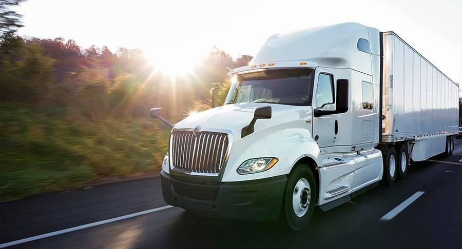 A white semi-truck drives down the road at sunset.