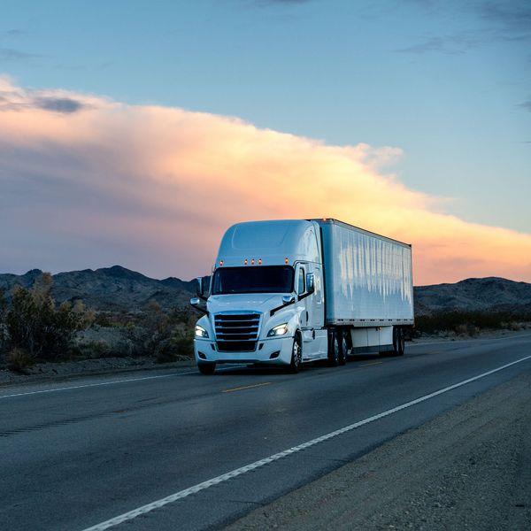 A white semi-truck drives up a road at sunset.