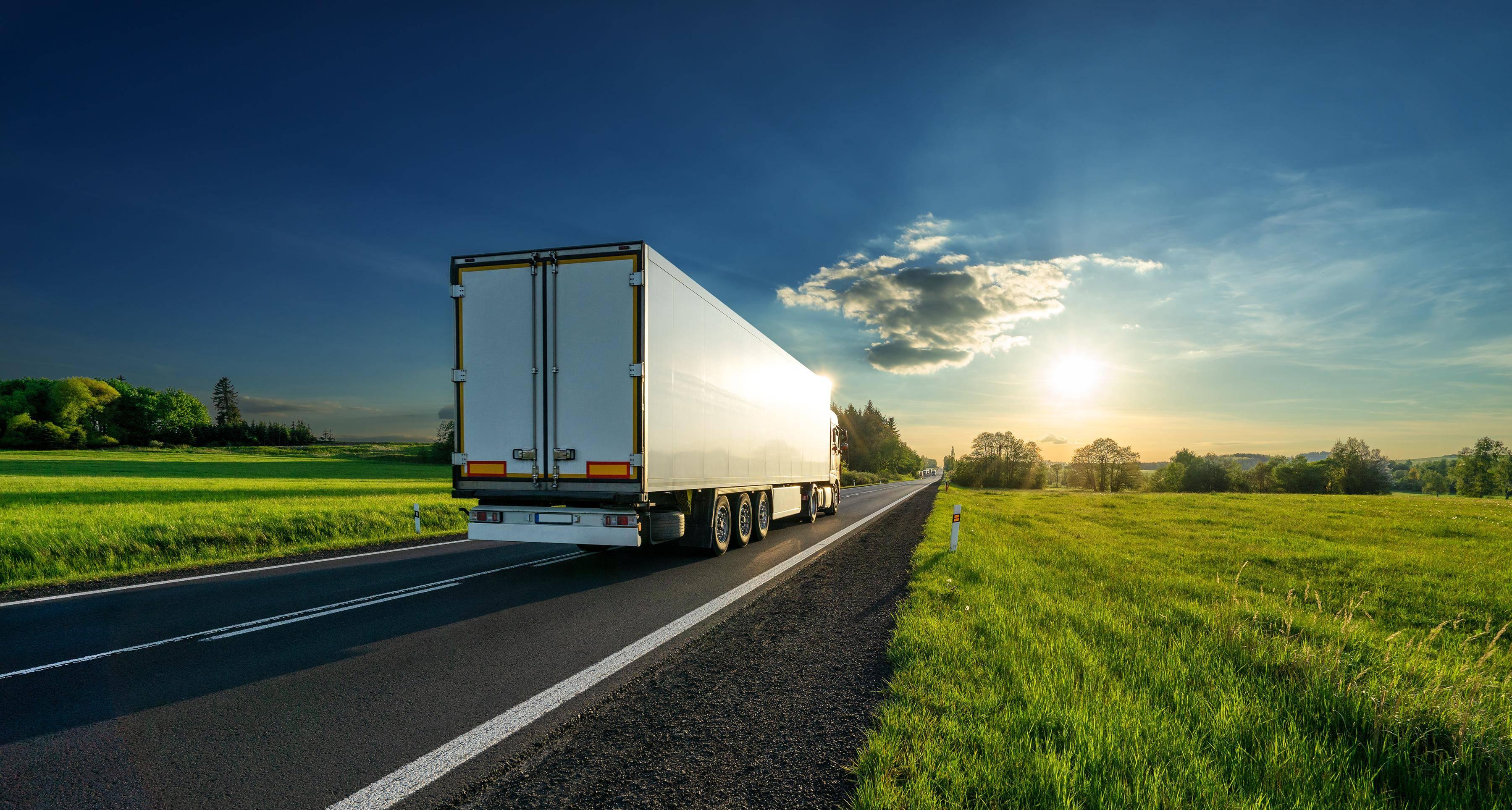 A white truck driving down a road in summer.