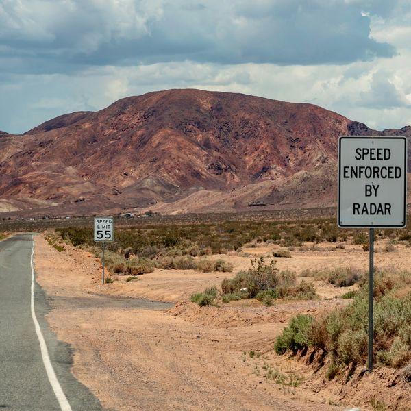 An empty desert road with a Speed Enforced By Radar sign.