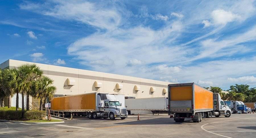 Multiple trucks maneuver around a warehouse yard.