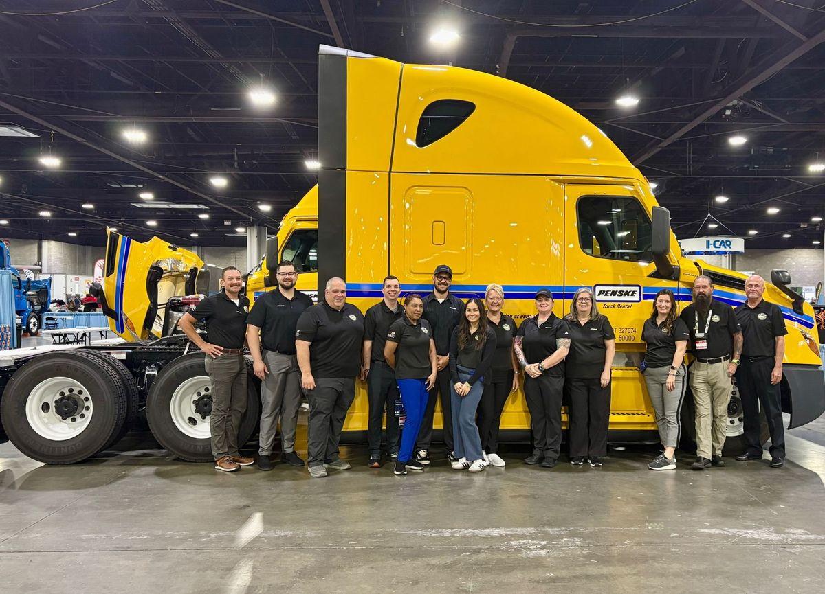 Penske employees lined up in front of a yellow Penske truck