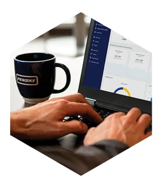 Person typing on a laptop in a cafe with a Penske mug