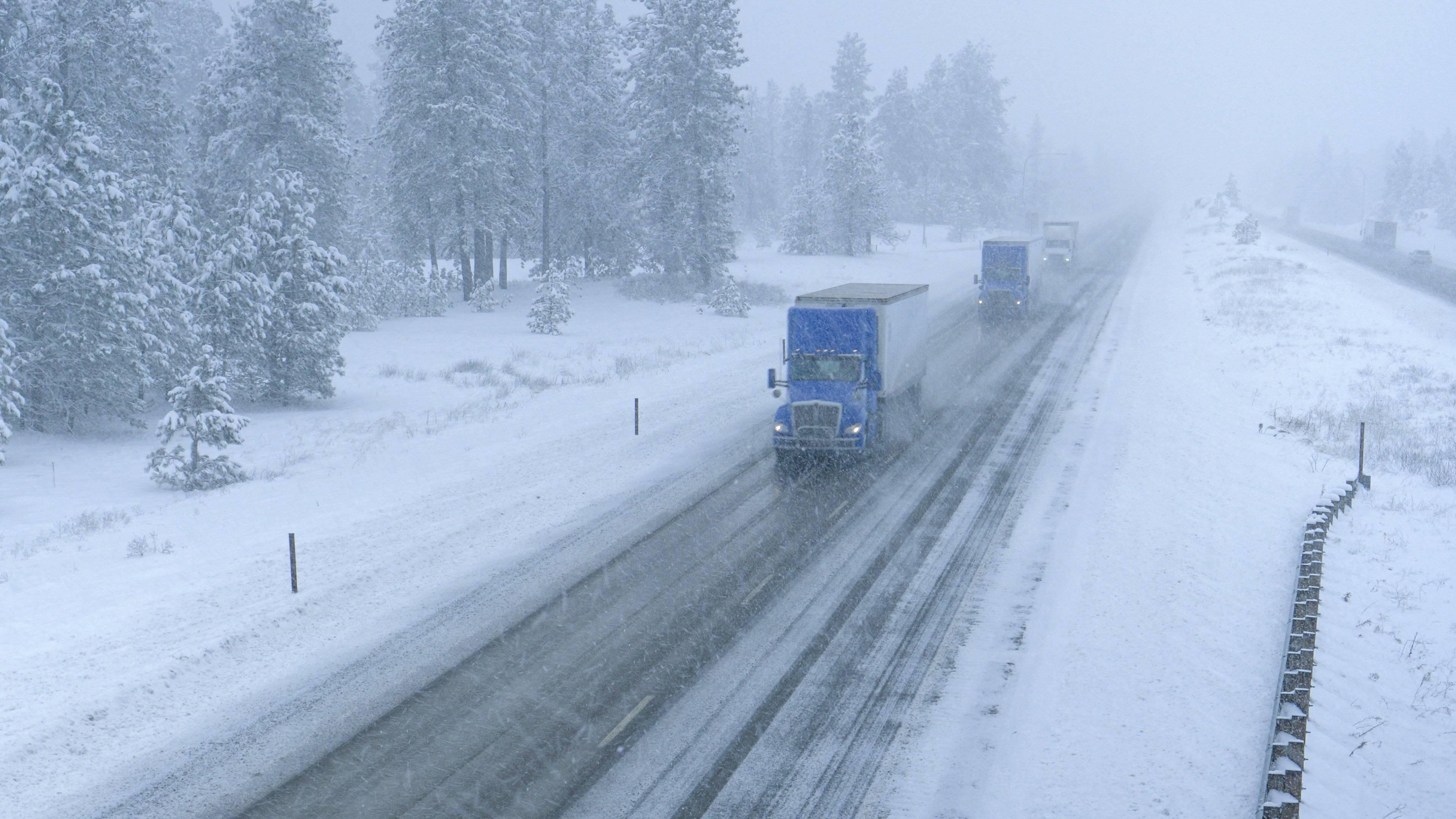 Three semi-trucks drive up a snowy road on a winter day.