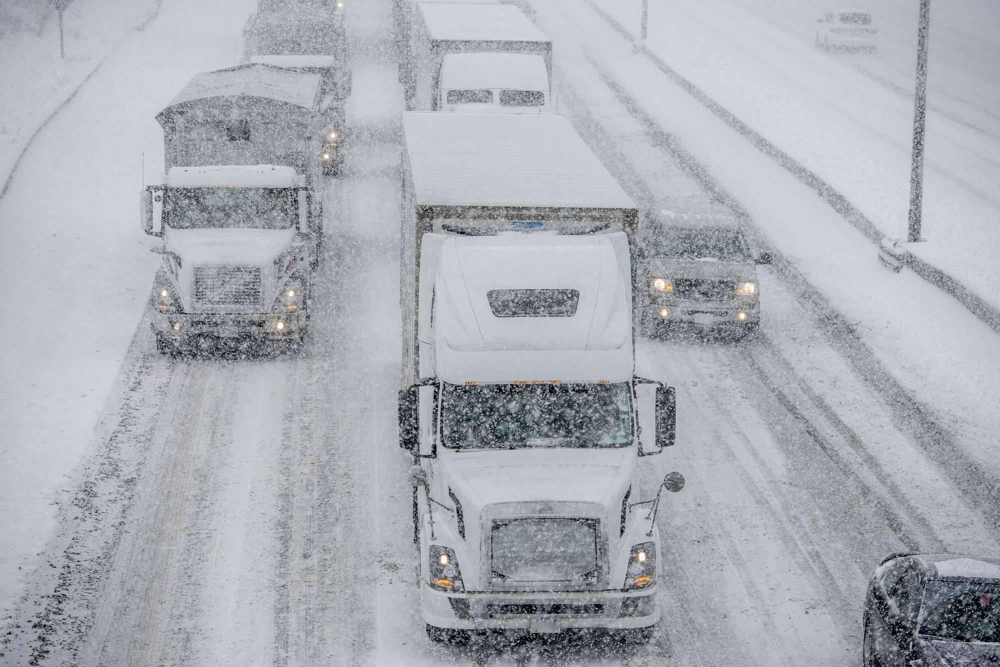 Trucks and cars drive on very snowy roads while it snows.