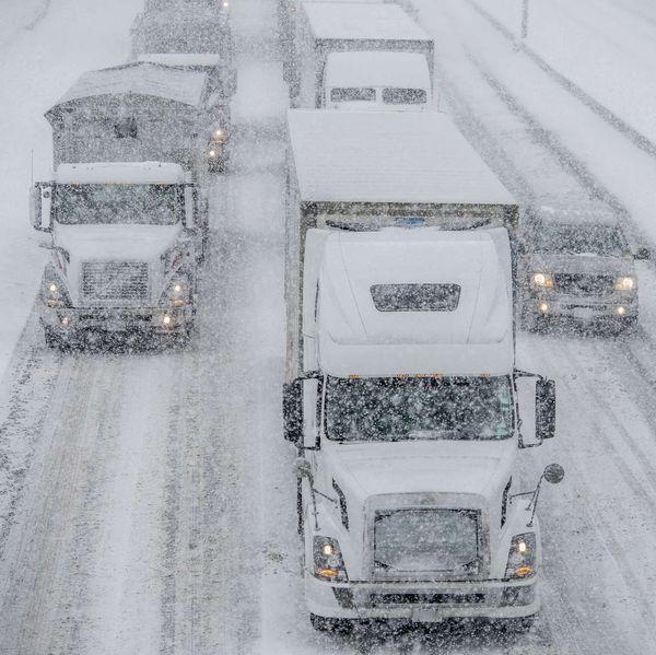 Trucks and cars drive on very snowy roads while it snows.