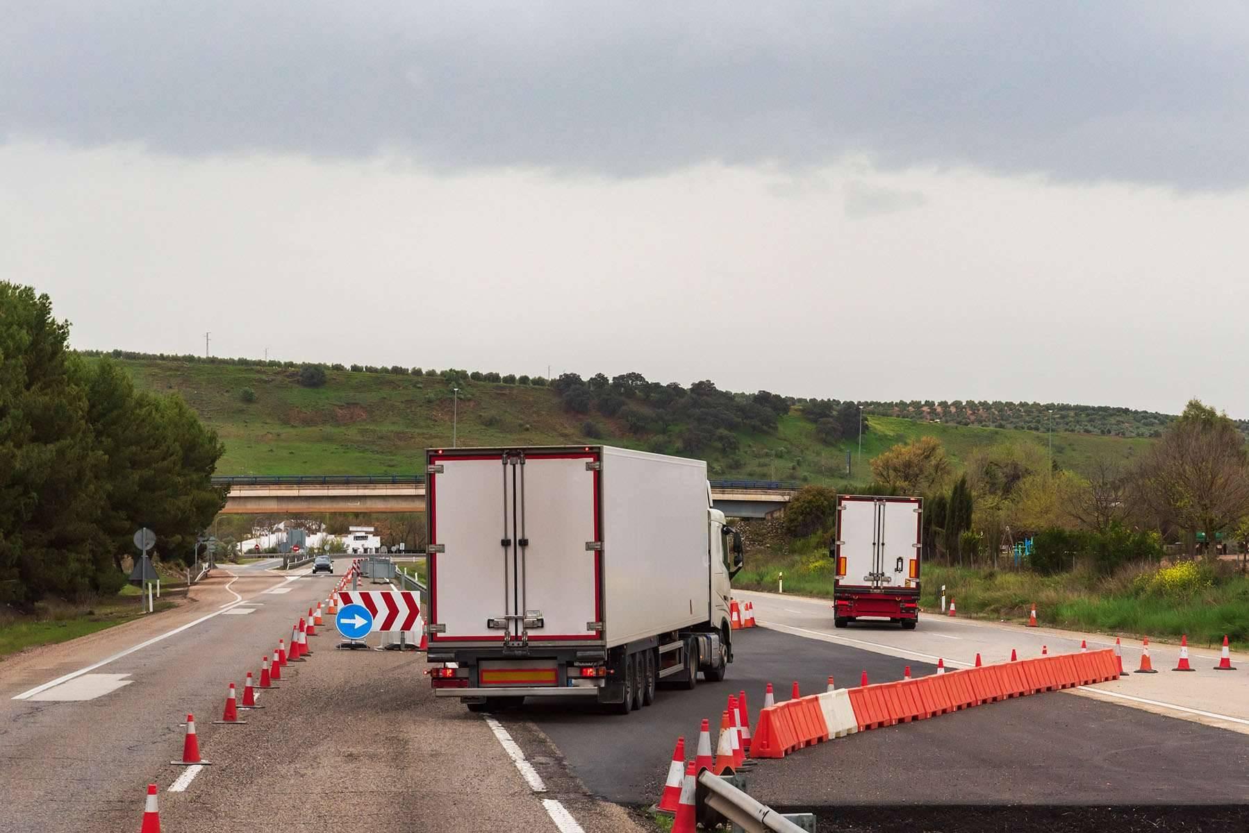 Two semi-trucks travel through a construction zone on a freeway.