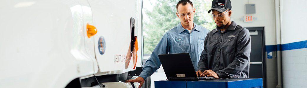 Two technicians by truck performing diagnostics with laptop