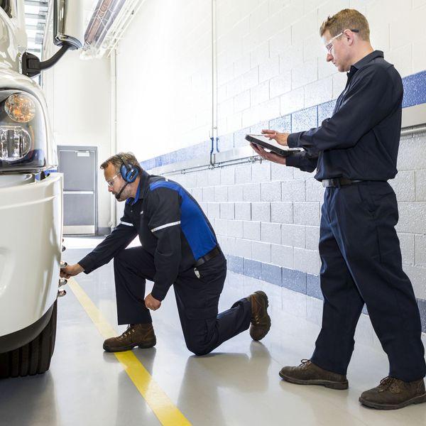 Two technicians check the alignment on a semi-truck wheel.