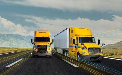 Two yellow Penske trucks driving down the highway