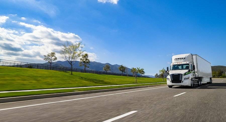 White electric Penske tractor-trailer drives on a sunny day.